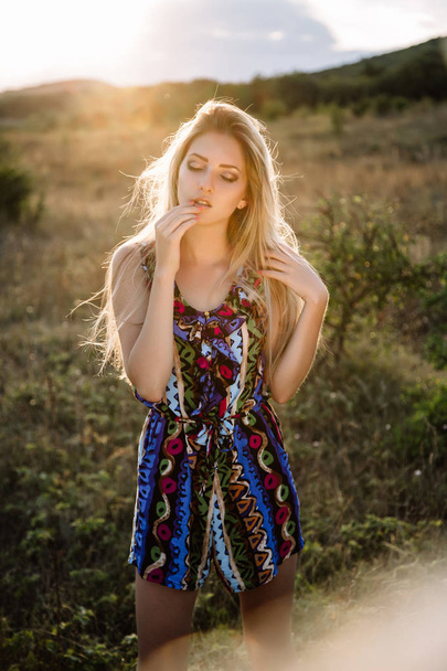 Beautiful blonde with beautiful eyes in blue overalls in nature, sunset sun - Fotografie, Obrázek