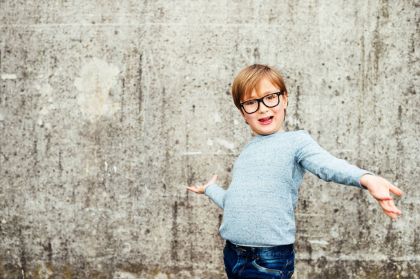 Outdoor portrait of a cute little boy wearing eyeglasses, light blue pullover and denim jeans - Photo, Image