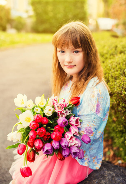 Outdoor portrait of a sweet kid girl with big bouquet of colorful tulips - Фото, изображение