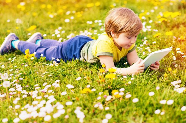 Onnellinen pieni lapsi poika pelaa tablet PC ulkona puistossa hyvin aurinkoinen päivä
 - Valokuva, kuva