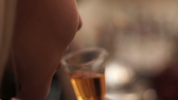 Tyttö juo viskiä pienestä lasista baarissa. Blondi tyttö maistaa konjakkia baarissa
 - Materiaali, video