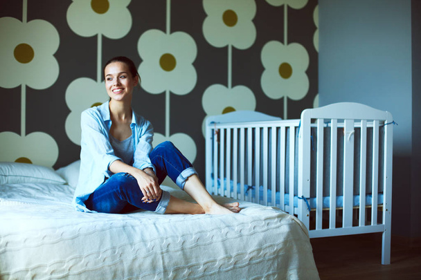 Young woman sitting on the bed near childrens cot - Fotoğraf, Görsel