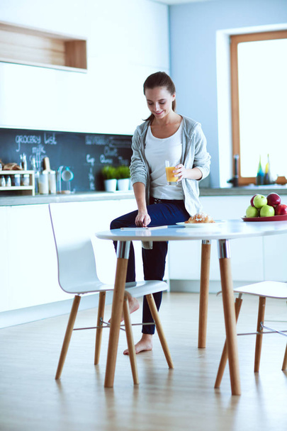 Young woman with orange juice and tablet in kitchen - Foto, Imagen