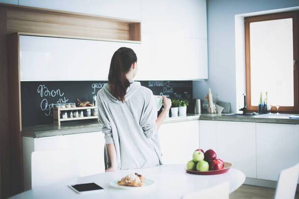 Happy woman drinking tea in the kitchen at home - 写真・画像