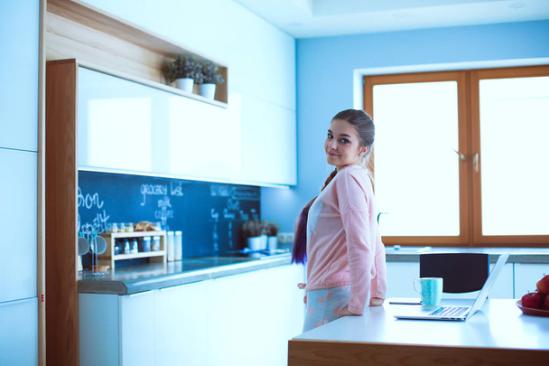 Жінка використовує мобільний телефон, що стоїть на сучасній кухні
 - Фото, зображення