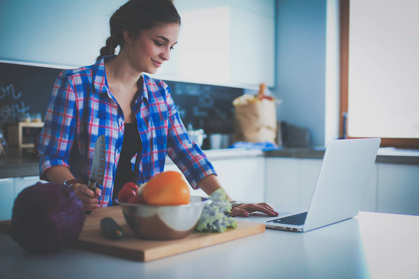 Young woman cutting vegetables in kitchen near desk - Zdjęcie, obraz