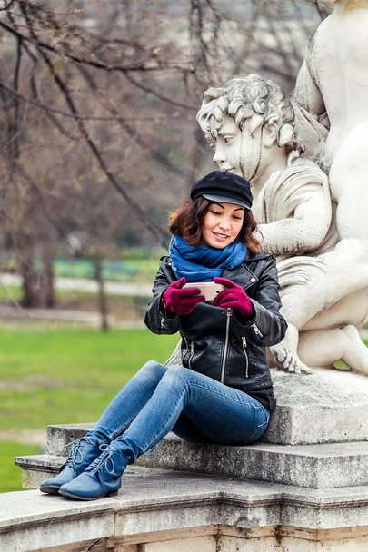 Fiatal női utas, így selfie a szobor Ámor szúró telefon, tavaszi kert és park - Fotó, kép