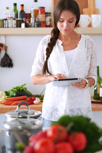 Young woman using a tablet computer to cook in her kitchen - Фото, изображение