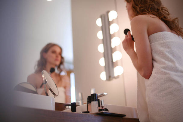 Young woman looking in the mirror and putting make-up on - Photo, image