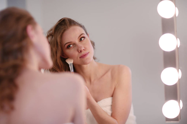 Young woman looking in the mirror and putting make-up on - Foto, immagini