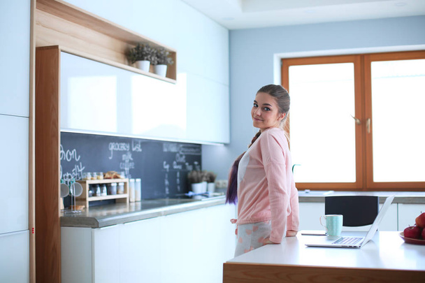 Woman using mobile phone standing in modern kitchen - Foto, afbeelding