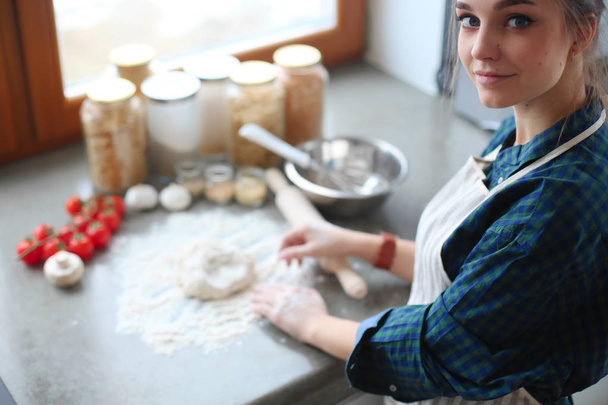 Beautiful woman cooking cake in kitchen standing near desk - Foto, Bild