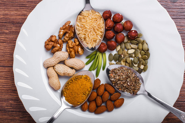 Assorted nuts in white bowl, plate on wooden surface. Top view with copy space - Foto, Imagem
