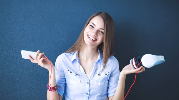 Smiling girl with headphones sitting on the floor near wall - Fotó, kép