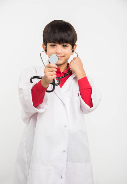 indian cute boy or kid in doctor's uniform with stethoscope and piggy bank in hand - Foto, afbeelding