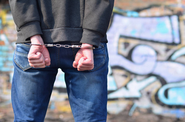 Rear view of the arrested and handcuffed offender against the graffiti background. The concept of preventing property damage, vandalism and combating hooliganism. anti-bullying concept - Photo, Image