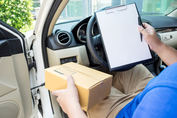 Доставщик с картонной коробкой проверяет список документов в фургоне и
 - Фото, изображение
