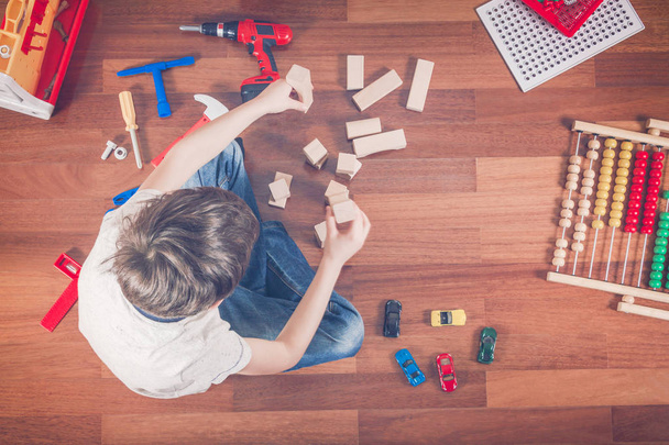 Niño jugando con juguetes mientras está sentado en el suelo de madera en su habitación.Vista superior
 - Foto, imagen