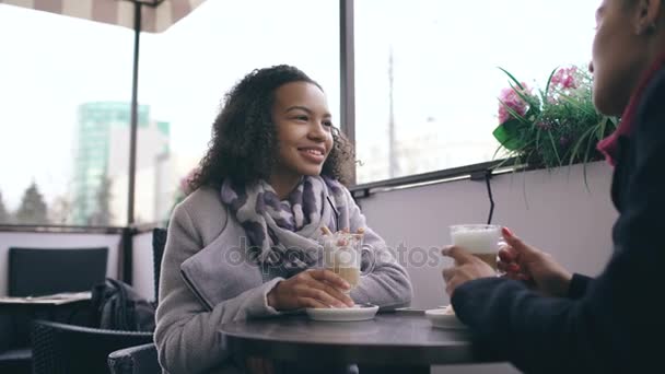 Δύο ελκυστικά μικτή φυλή γυναίκες μιλάμε και πίνοντας καφέ στην καφετέρια του δρόμου. Φίλοι να διασκεδάσουν μετά την επίσκεψη πώληση εμπορικό κέντρο - Πλάνα, βίντεο