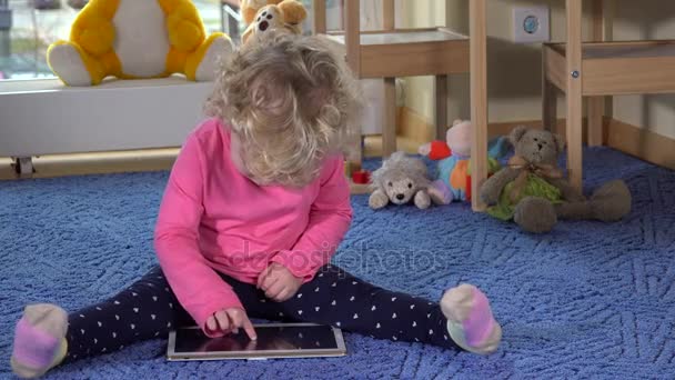Little caucasian girl using tablet pc sitting on blue carpet - Materiał filmowy, wideo