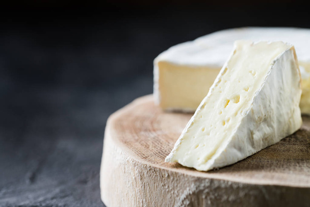 Primer plano de brie de queso blando cortado en rodajas de madera cortado sobre fondo rústico oscuro
 - Foto, imagen