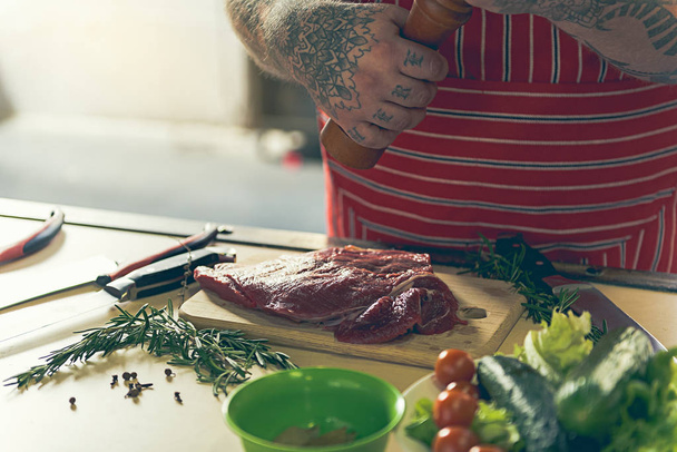 Fat man adding spices to fresh pork meat - Foto, immagini