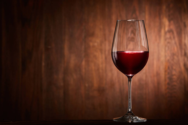Fragile goblet of the red wine on the wooden stand on wooden wall background. - Foto, afbeelding