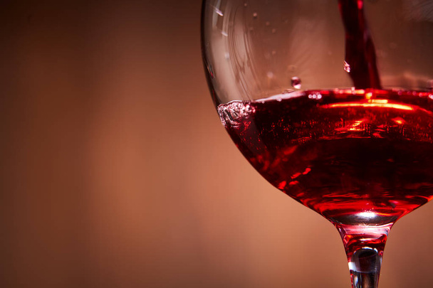 Close-up of brightly red wine poured in the wineglass and abstract splashing against brown background. - Foto, afbeelding
