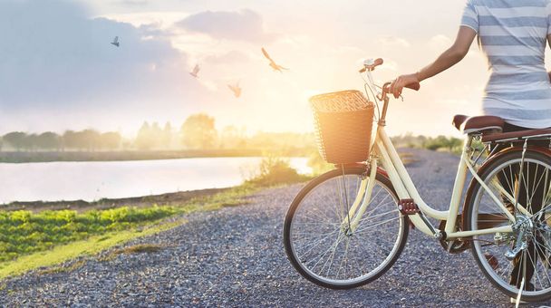 Frau steht mit Oldtimer-Fahrrad und entspannt im Sommer bei Sonnenuntergang in der Natur - Foto, Bild