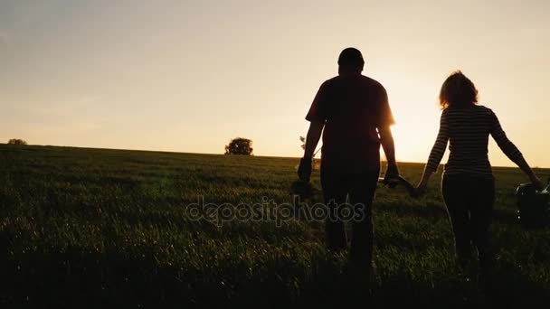 Steadicam výstřel: zemědělci - muž a žena kráčející po pole při západu slunce. Nést sazeničku stromu, konev a lopatu. Koncept - práce na zahradě, dobrovolnictví, nový život - Záběry, video
