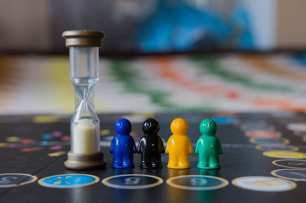 Fichas multicolores para juego de mesa en forma de hombrecitos y un reloj de arena
 - Foto, Imagen