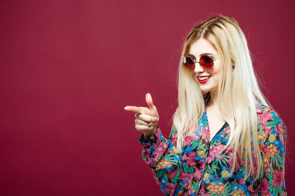 Cute Female Model with Sunglasses and Long Hair Wearing Colorful Shirt on Pink Background. Amazing Blonde is Posing in Studio. - Photo, Image