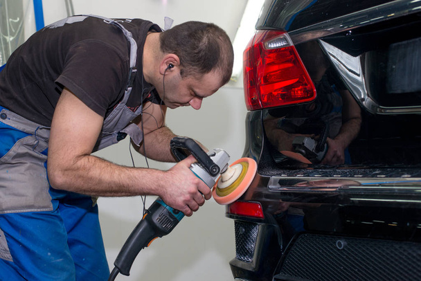 A man polishes a black car with a polishing machine - Фото, зображення