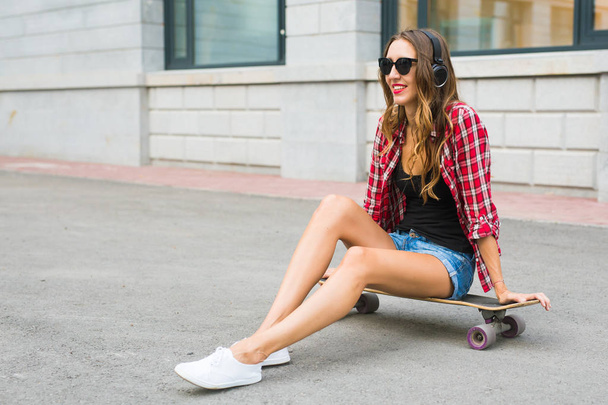 Young woman sitting on the skater. Smiling woman with skateboard in outdoors - Photo, Image