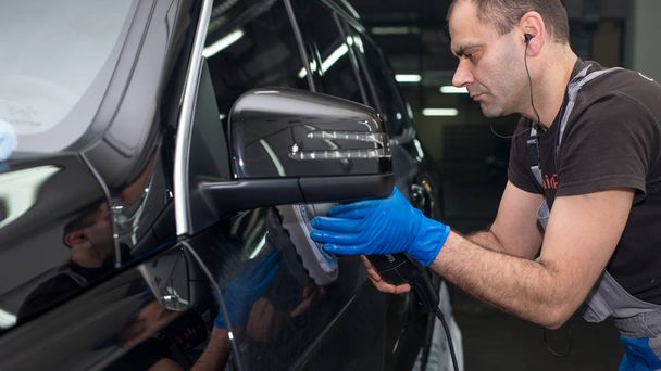 A man polishes a black car with a polishing machine - 写真・画像