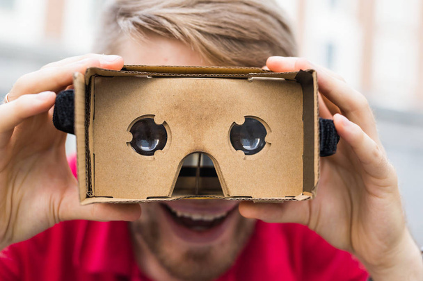 Funny man using cardboard virtual reality goggle outdoors - Fotó, kép