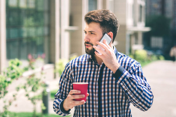 Handsome sporty bearded dark-haired man Drinking coffee and talking on the phone - Foto, imagen