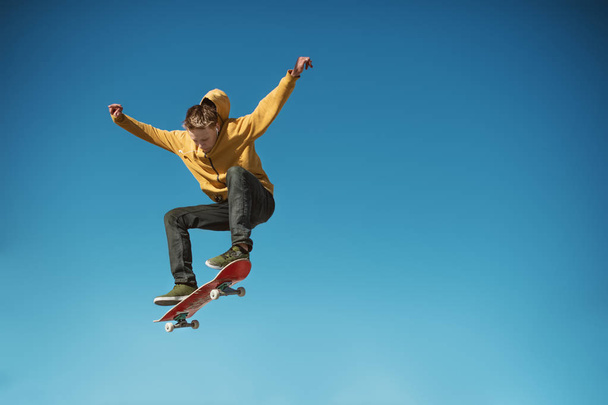 Een tiener skateboarder doet een truc van de ollie op achtergrond van blauwe hemel verloop - Foto, afbeelding