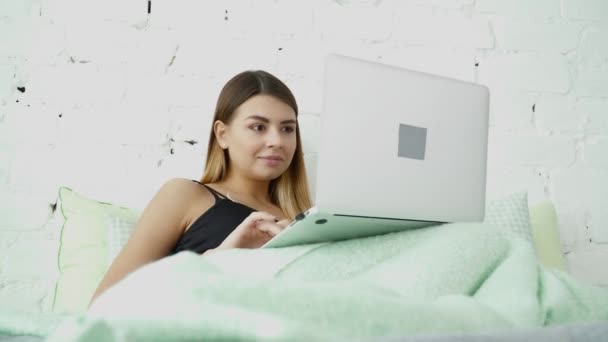 Young beautiful woman using her laptop in the bed - Πλάνα, βίντεο