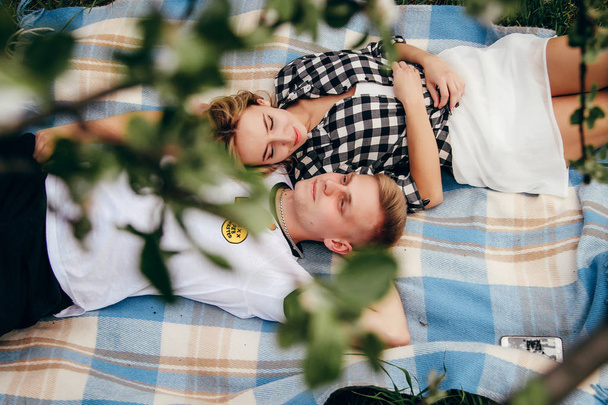 Familienfoto. Mann und Frau liegen auf einer karierten Matte im Apfelgarten. Sie schauen einander an, lächeln und küssen sich. auf dem Foto herrscht eine Atmosphäre der Liebe, Ruhe und des Glücks - Foto, Bild
