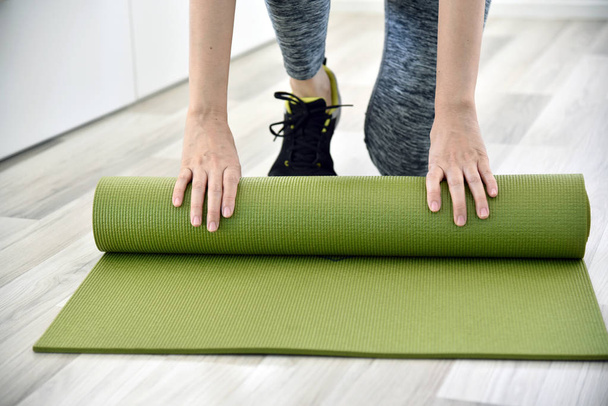 Woman folding yoga or fitness mat after working out at home, Home exercise workout. - Fotografie, Obrázek