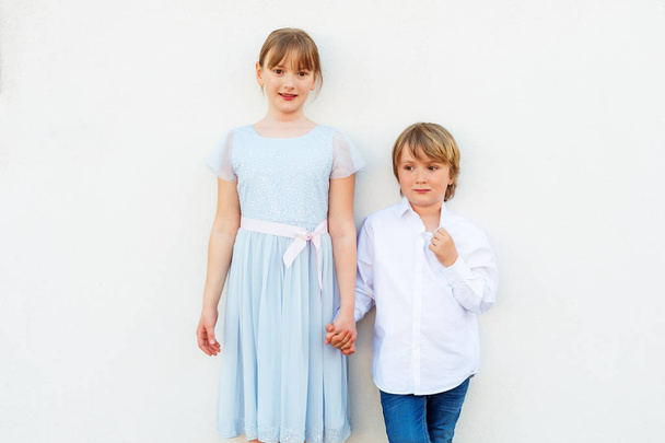 Grupo de dos niños, niña y niño, con ropa de fiesta, de pie sobre fondo blanco
 - Foto, Imagen