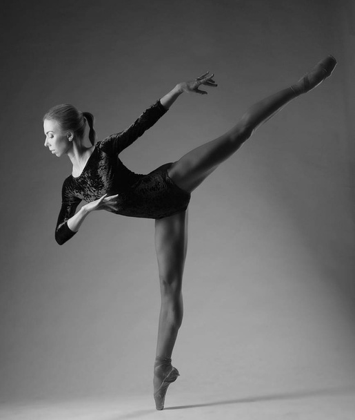 Ballerina in black outfit posing on toes, studio shot. on one leg, black and white image - Фото, изображение