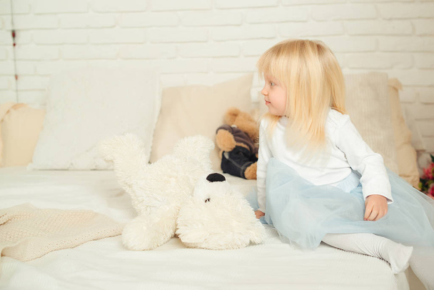 Cute toddler girl sitting on the bed with her soft toys in a light room. Happy birthday concept. - Foto, imagen