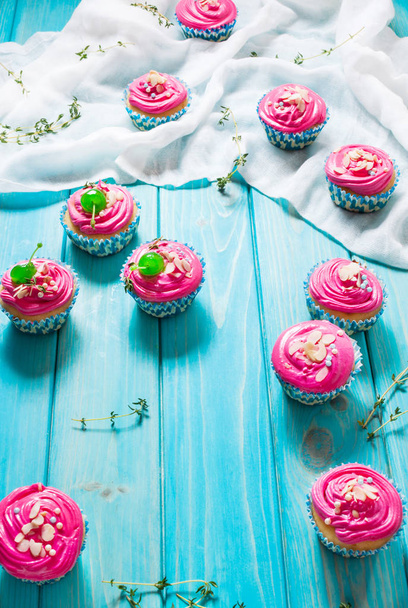 青い木製の背景にカラフルなピンクのカップケーキ - 写真・画像