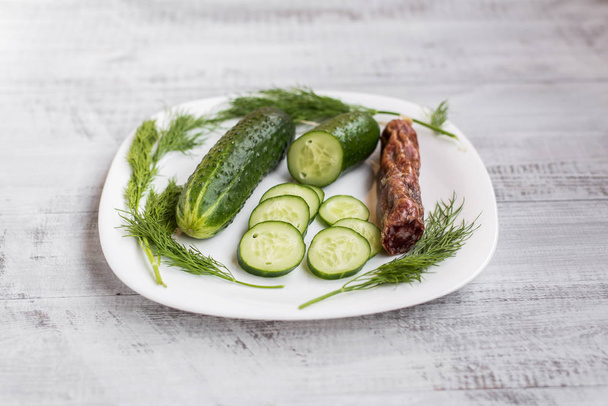 Cucumber, tomato, dill and sausage on a wooden table. Sliced cucumber. - Fotografie, Obrázek