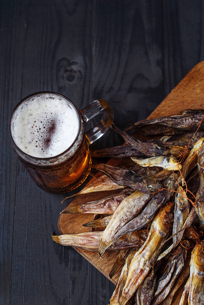 A glass of beer with dried fish. Light beer with sea Bullhead. Goby and beer on a dark background - Photo, Image