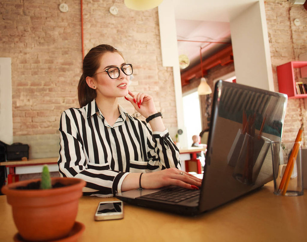 Thoughtful business woman at table in office working at laptop - Photo, Image