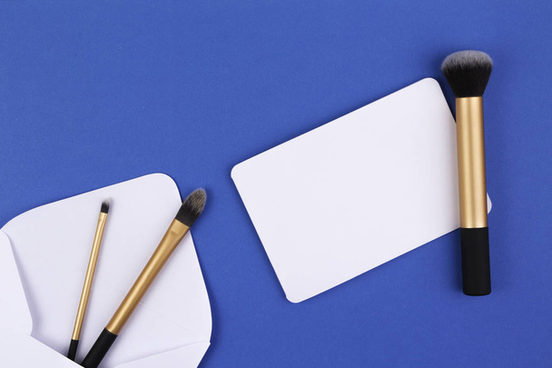 Make up brushes and white envelope with blank card on blue background - Photo, Image