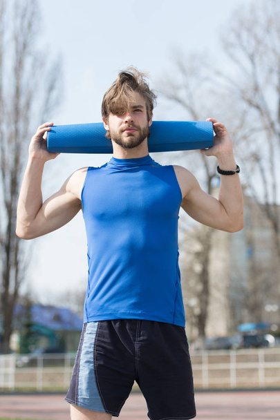 Yoga, fitness mat blauw kleur in handen van gespierde man - Foto, afbeelding